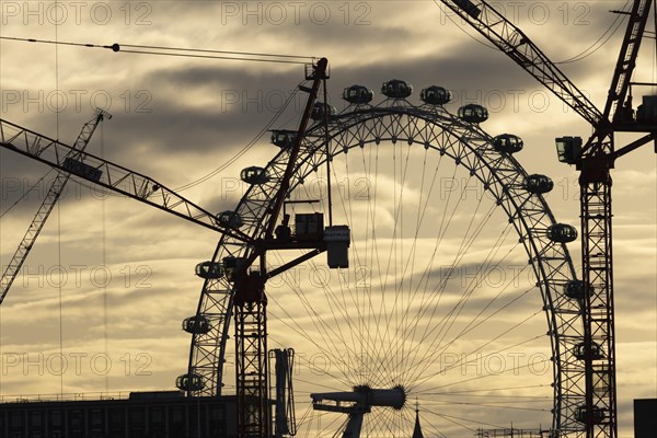 London Eye or Millennium Wheel tourist observation wheel at sunsetwith industrial cranes and cityscape in the foreground, City of London, England, United Kingdom, Europe