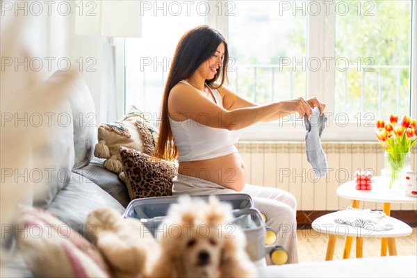Happy pregnant woman folding clothes preparing bag to the hospital to childbirth