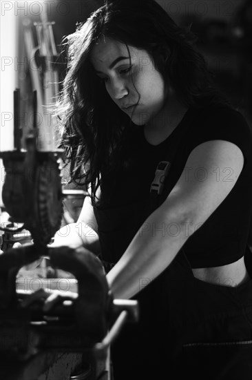 Hispanic latino long haired brunette sexy woman mechanic examining a car part in a well-equipped workshop, a complete tool panel in the out of focus background with bokeh effect