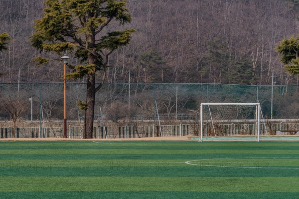 Empty soccer field with a single goal post and trees in the background, in South Korea