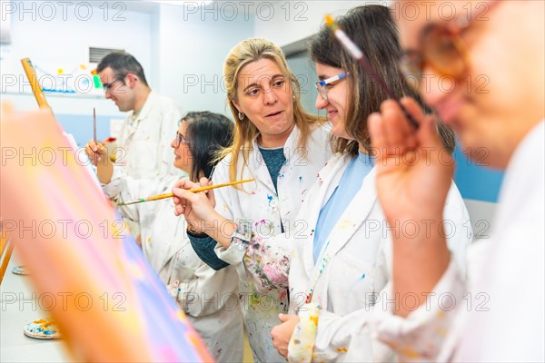 Art instructor teaching and talking to a disabled woman painting on canvas