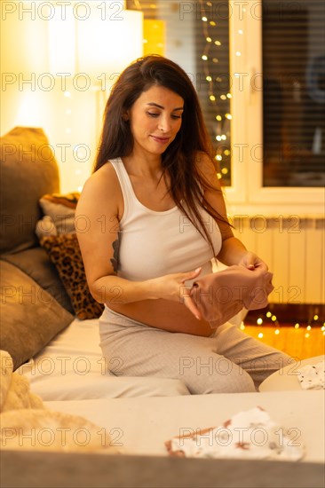 Vertical portrait of a tranquil scene of a beauty pregnant woman folding clothes preparing bag for childbirth at night