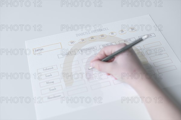 Diabetes log, daily log of food and insulin administration, food log, hand of a child holding a pen and appearing to fill in the log, the paper lies on a white table, Ruhr area, Germany, Europe