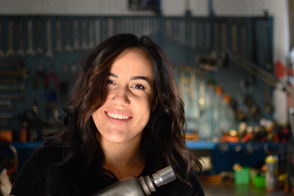 Joyous woman mechanic laughing in a workshop environment, a complete tool panel in background with bokeh effect, traditional male jobs by Mixed-race latino female