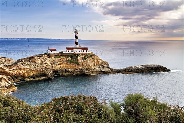 Lighthouse standing on rocky cliffs surrounded by calm sea waters at dusk, Coastal Hiking tour in the south of Mallorca