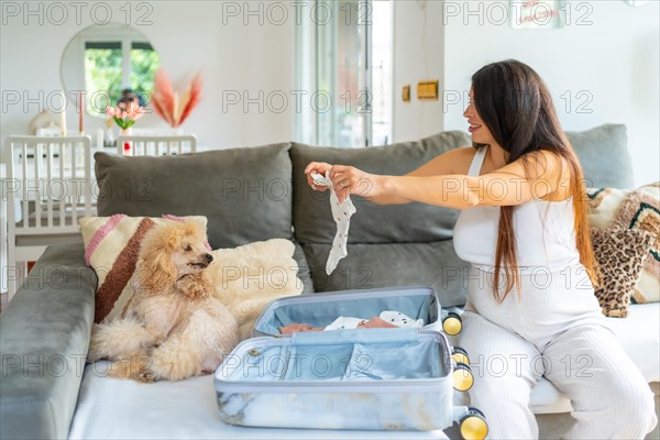 Pregnant woman preparing bag for the hospital for childbirth in the sofa with a dog next to her