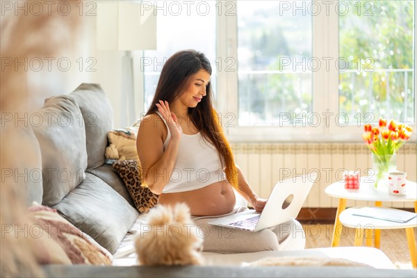 Pregnant woman waving during video call at home with her gynecologist