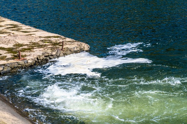 Suds and foam gather at the concrete edge of a water body with visible waves, in South Korea