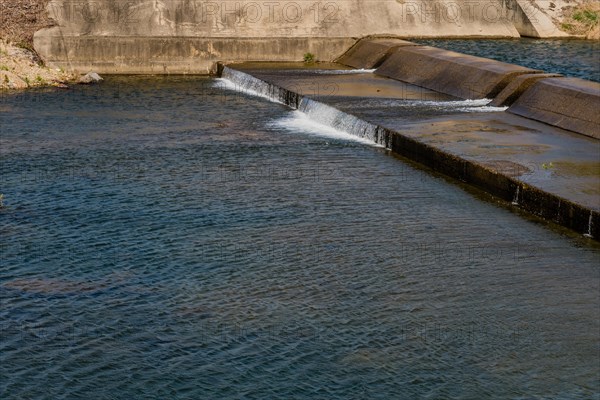 Bright daylight captures water flowing smoothly over a concrete overflow structure, in South Korea