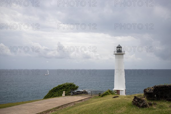 White lighthouse on a steep coast. Dramatic clouds with a view of the sea, pure Caribbean at Le Phare du Vieux-Fort, on Guadeloupe, French Antilles, France, Europe