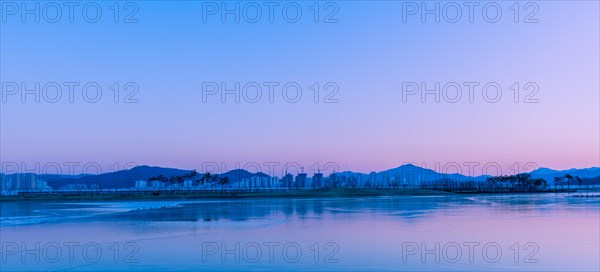 Pastel skies at twilight reflect over a serene lake with silhouetted landscape, in South Korea