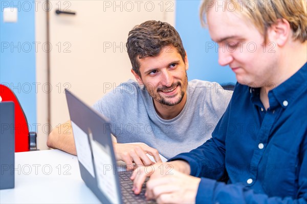 Friendly handsome teacher helping an adult disabled man during computing class