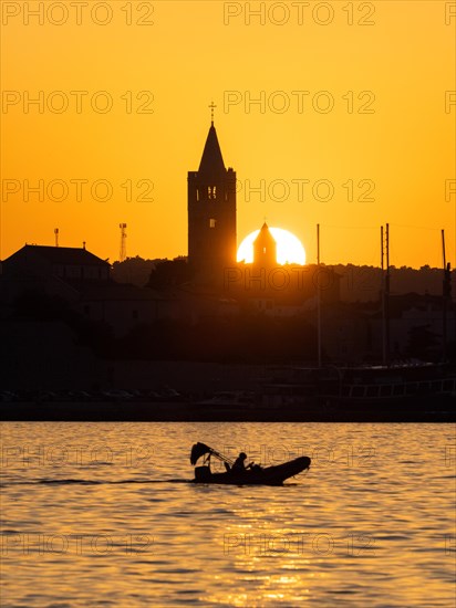 Motorboat in the golden evening light at sunset, silhouette of the church towers of Rab, town of Rab, island of Rab, Kvarner Gulf Bay, Croatia, Europe