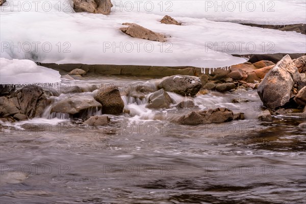 Tranquil stream with areas of snow and scattered boulders, in South Korea