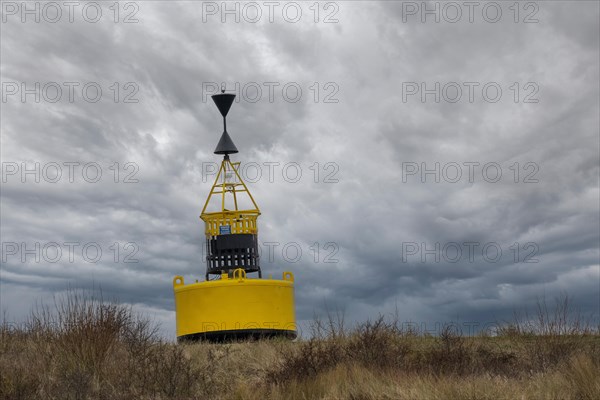 A bright yellow navigation mark stands in the landscape against a dramatic cloudy sky