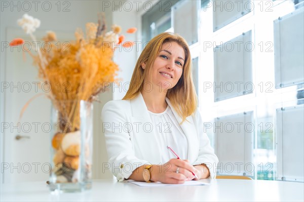 Smiling estate agent taking notes while looking at camera working in the office
