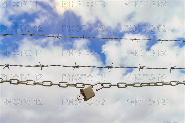 Chain with padlock open with key next to a barbed wire with a blue cloudy sky with sun rays, concept of freedom