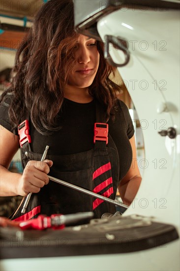Hispanic young sensual long haired brunette Female mechanic attentively working with a screwdriver repairing a vintage italian scooter, latino woman in traditional masculine jobs concept, feminine power in real life