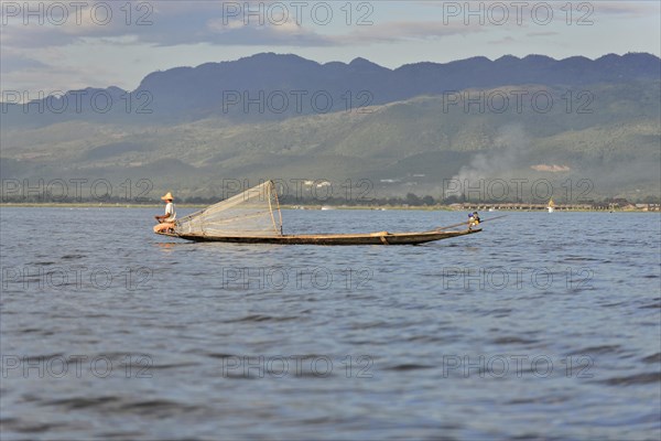 Fisherman on a boat prepares his net, surrounded by a lake landscape, Inle Lake, Myanmar, Asia