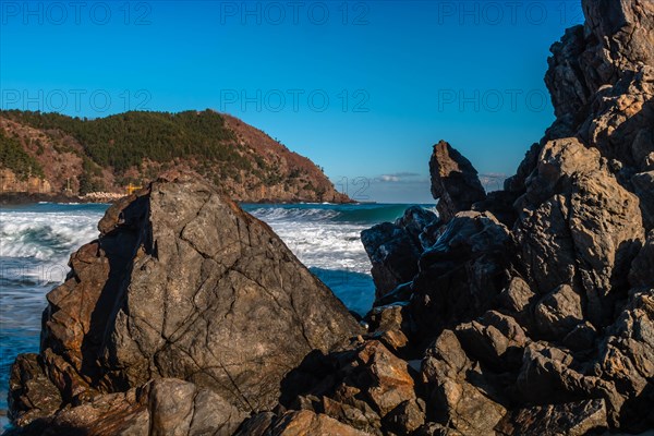 Frothy ocean waves kiss the rocky landscape under the expansive blue skies, in South Korea