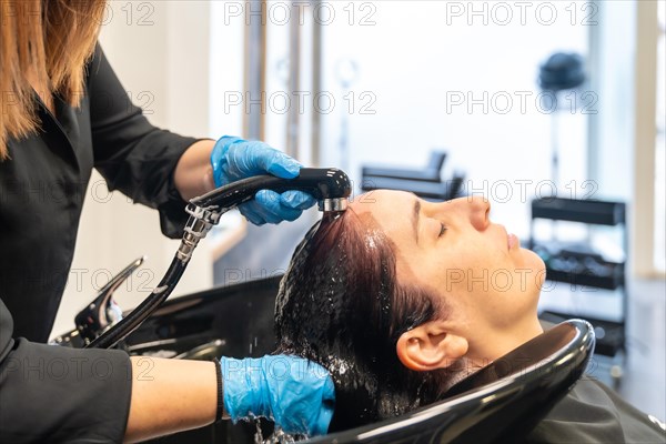 Relaxed woman with eyes closed washing her hair in a beauty hair salon