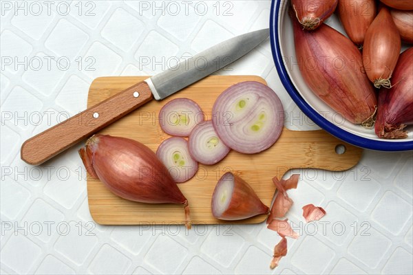 Shallots on wooden board with knife, Allium cepa