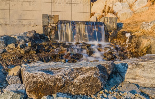 A man-made waterfall flows gently over sunlit rocks, in South Korea