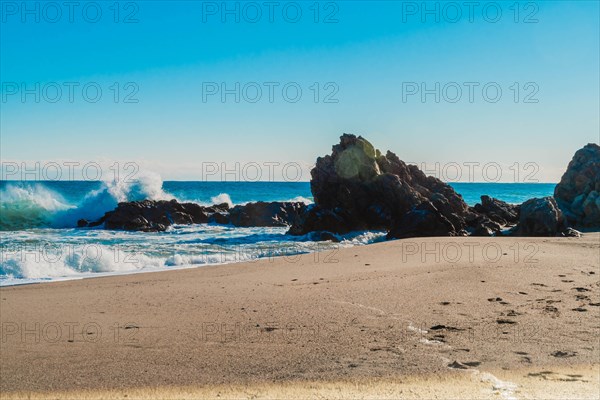Gentle waves meet the sandy beach with prominent rocks and clear blue sky, in South Korea