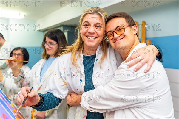 Portrait of a happy man with down syndrome embracing his painting teacher during class