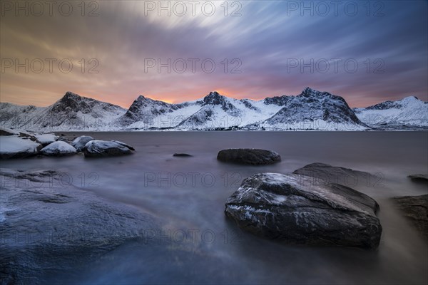 Rocky coast at the fjord with snow-covered mountains at sunset, Steinfjorden, Tungeneset, Husfjellet, Senja Island, Norway, Europe