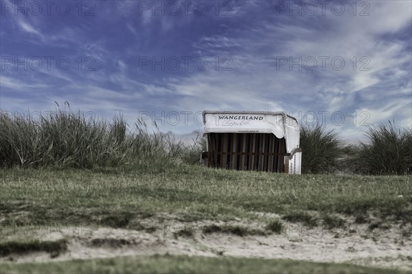 Beach chair Wangerland, standing on the beach of Schillig in the dunes, surrounded by green meadows, background bright blue sky with clouds, Schillig, Wangerland, North Sea coast, Germany, Europe