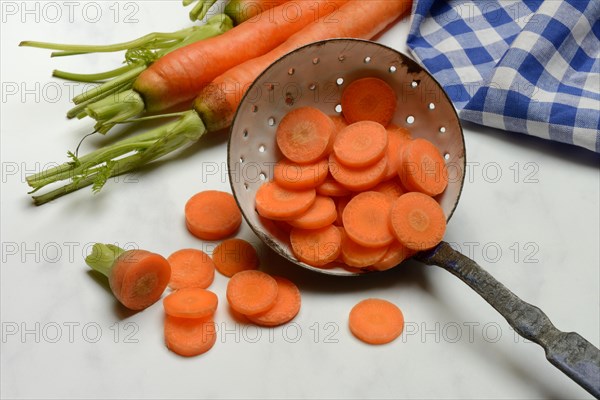 Carrot slices in colander and wooden spoon, Daucus carota