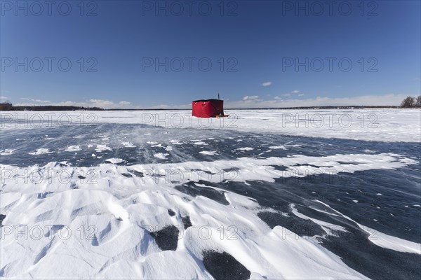 Winter, red fishing hut with snow drifts on a frozen riverscape, Saint Lawrence River, Province of Quebec, Canada, North America