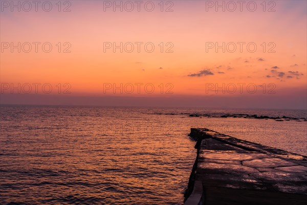 A wooden pier stretches into the sea under a golden sunset sky, in South Korea