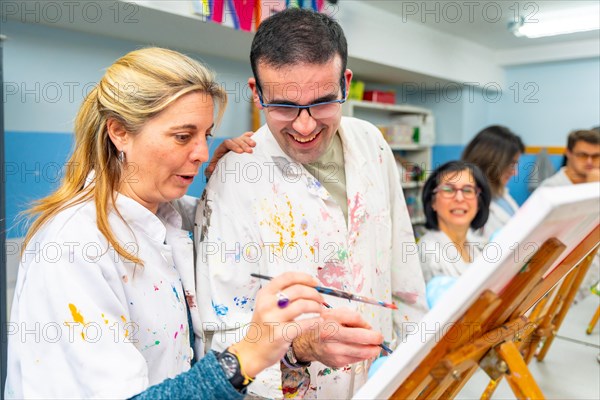 Instructor helping a disabled man during painting class in a center for people with special needs