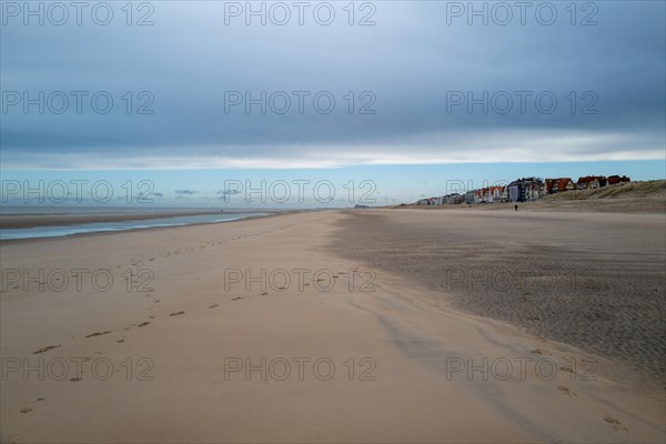 Disused beach with dunes in the background and houses on the horizon under a cloudy sky, DeHaan, Flanders, Belgium, Europe