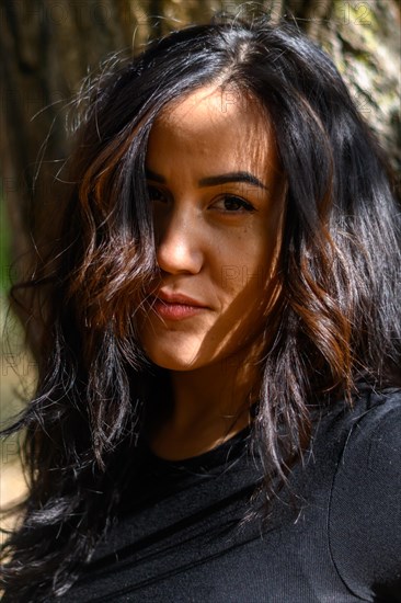 Portrait of a Cheerful hispanic young woman with curly hair in dappled sunlight outdoors, blurred background with bokeh, daytime, AI generated