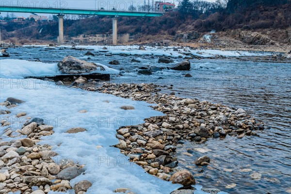 Meandering river with scattered stones and ice, bridge in the distance, in South Korea
