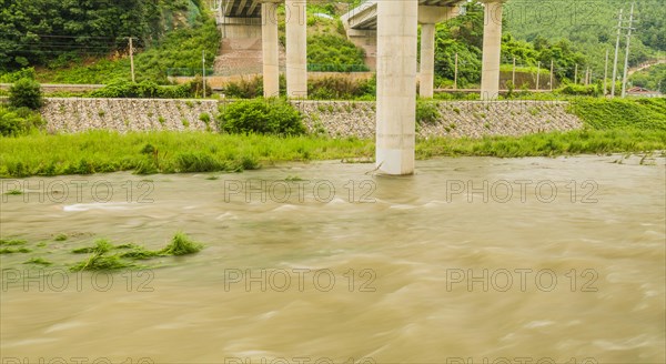 Swift green river flowing under the pillars of a bridge with cloud-covered skies, in South Korea