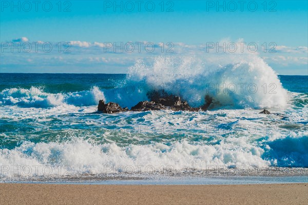 Dynamic white waves collide with coastal rocks on a sunny day with a vibrant blue ocean, in South Korea