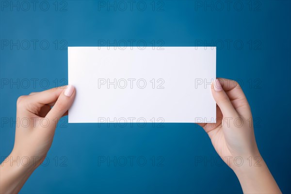 Female hands holding up empty white note in front of blue background. KI generiert, generiert AI generated