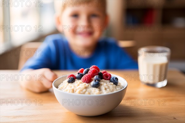 Table with bowl with healthy breakfast oatmeal porridge with berry fruits and happy smiling young boy child in background. KI generiert, generiert AI generated