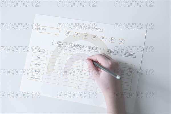 Diabetes log, daily log of food and insulin administration, food log, hand of a child holding a pen and appearing to fill in the log, the paper lies on a white table, Ruhr area, Germany, Europe