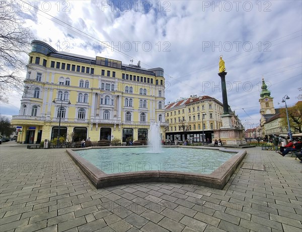 Graz, Austria, 26.03.2023: Mary's Column and fountain in Jakominiplatz Square and Parish Church in the background, famous attraction in the city center of Graz, Steiermark region, Austria, Europe