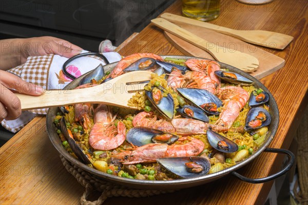 A person serving seafood paella with a wooden spatula from a traditional pan, typical Spanish cuisine, Majorca, Balearic Islands, Spain, Europe