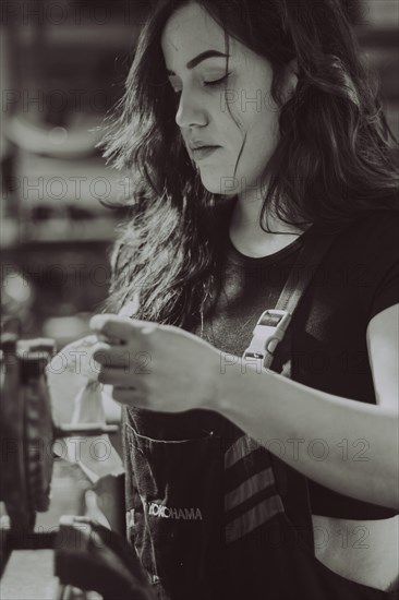 Focused woman inspecting an object during manual work in a workshop, real women performing traditional man jobs of the past, black and white photograph