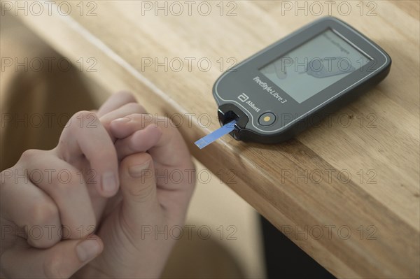 Blood glucose meter with test strips lying on a wooden table, child's hand holding a finger and guiding it to the meter, blood glucose measurement, diabetes treatment, glucose measurement, Ruhr area, Germany, Europe