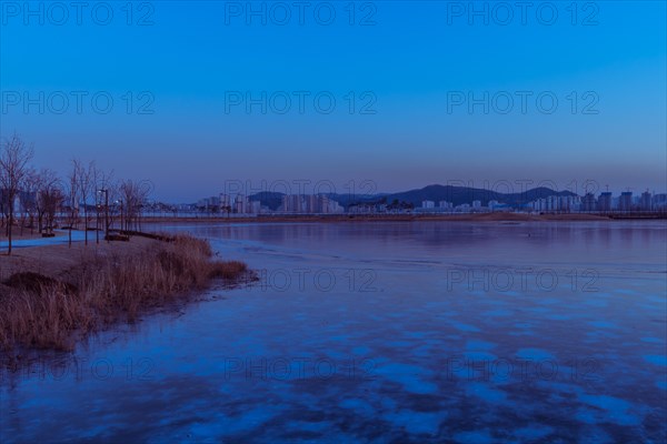 Serene dawn with a waterfront city skyline and ice in the foreground, in South Korea