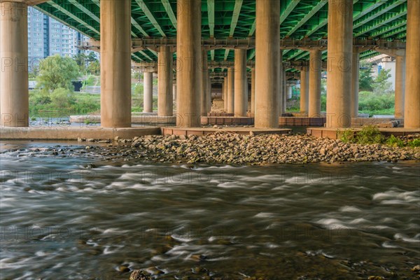 Long exposure shot of a river flowing under a green bridge with columns, in South Korea