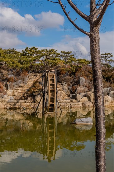 The serene reflection of a water wheel in clear pond water with trees and rocks, in South Korea